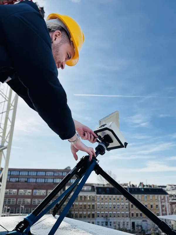 Teammitglied mit Schutzhelm kalibriert die Baustellenkamera auf dem Rooftop